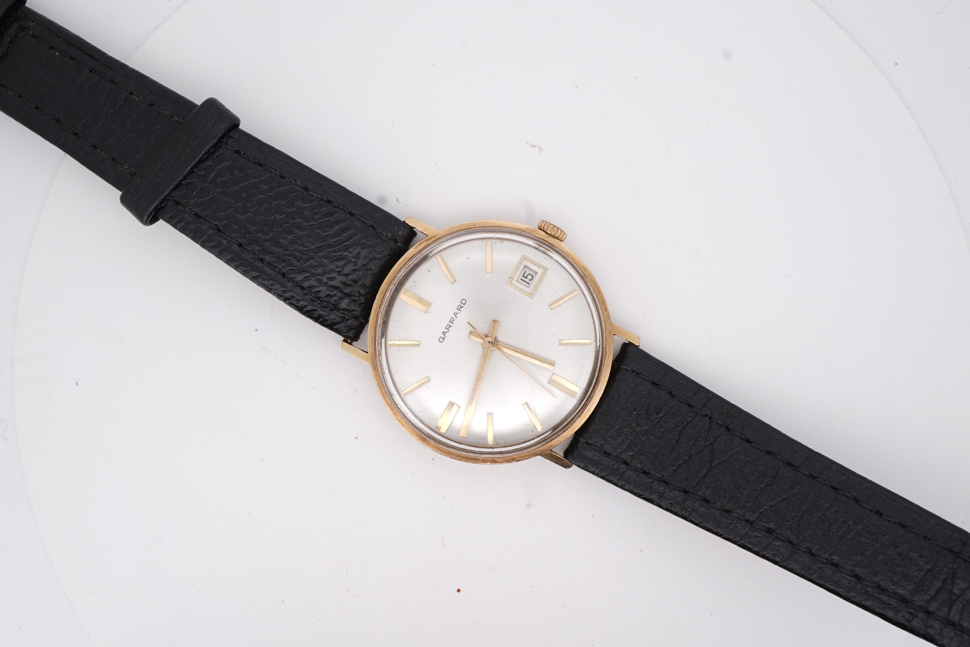A gentleman's yellow metal Garrard manual wind wrist watch, with baton numerals and date aperture, case diameter 34mm, on a black leather strap.